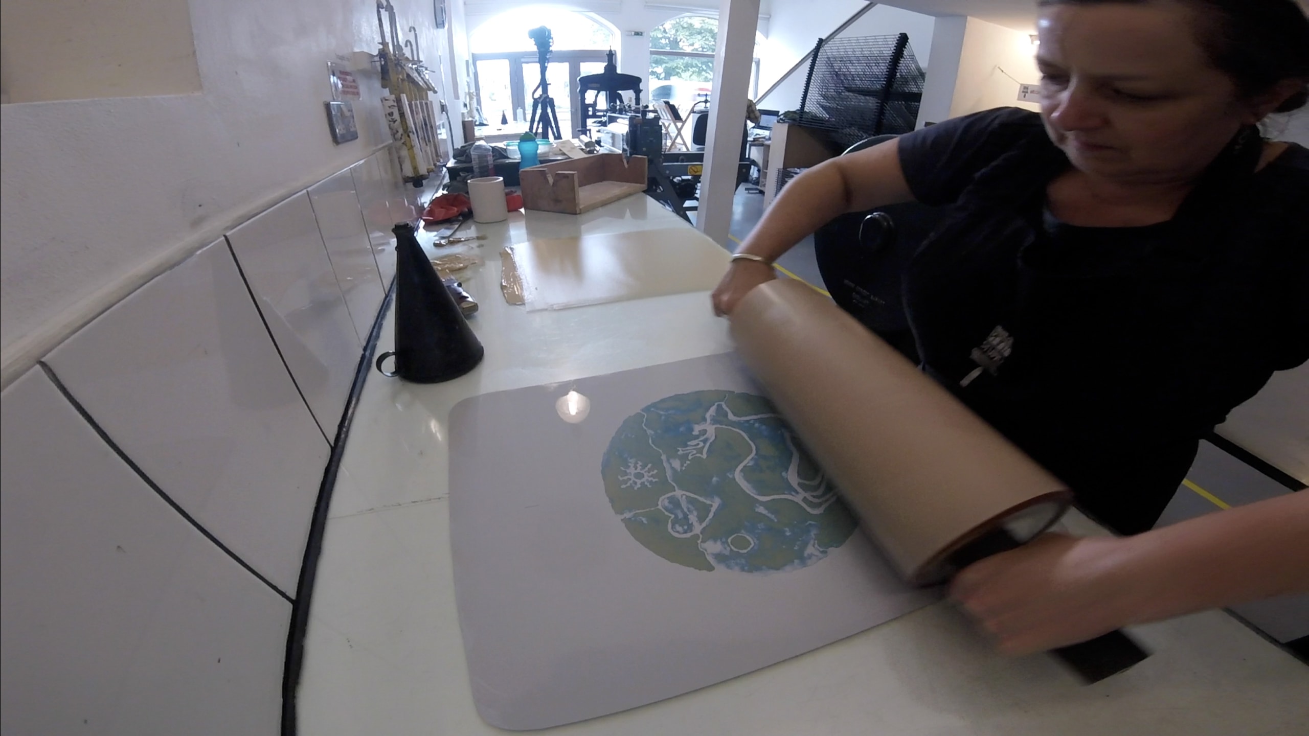 A photo lithography plate being printed by a woman rolling ink onto the stencil and paper beneath