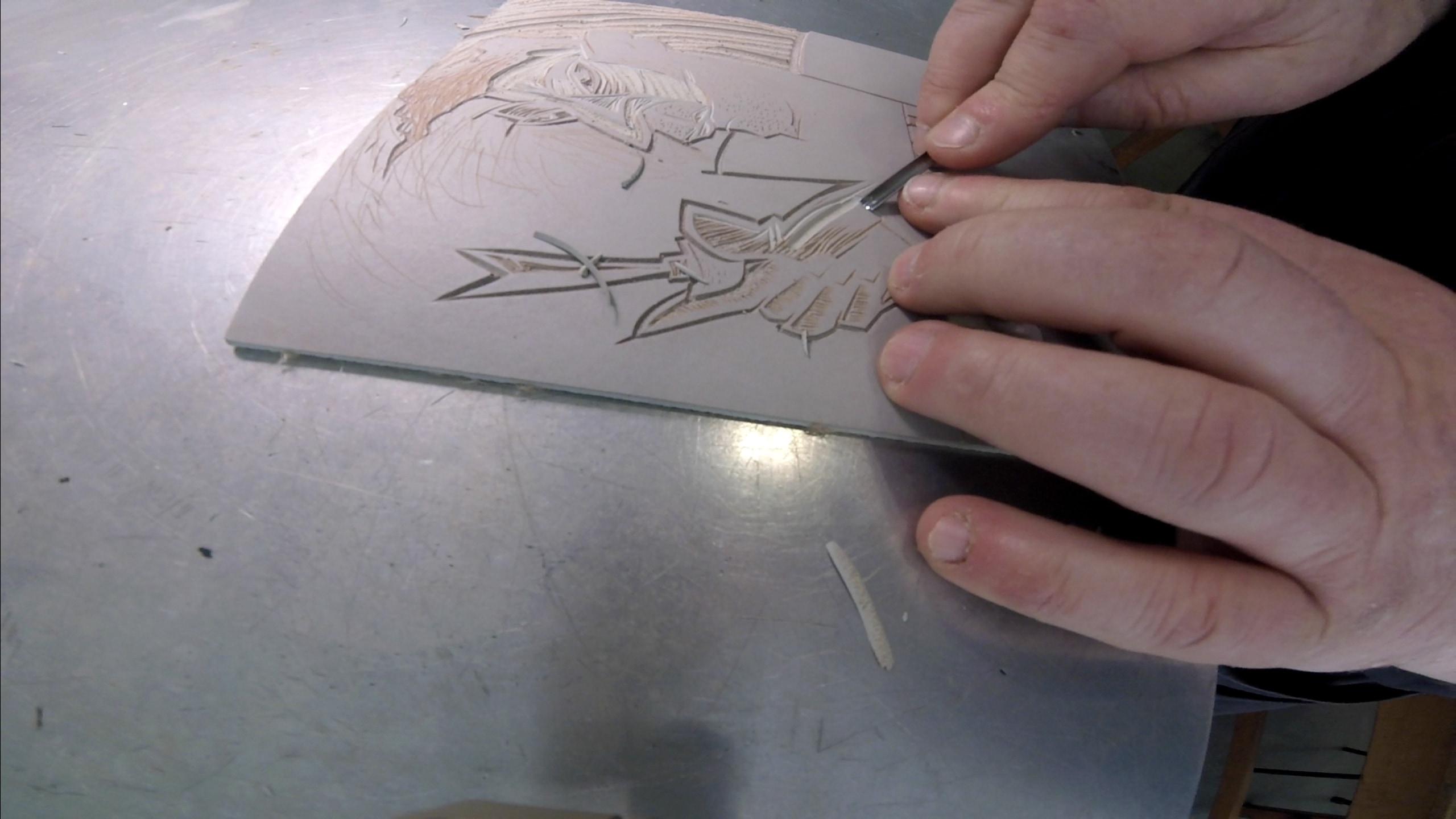 A relief print plate being designed by a person cutting out lines for the ink to flow