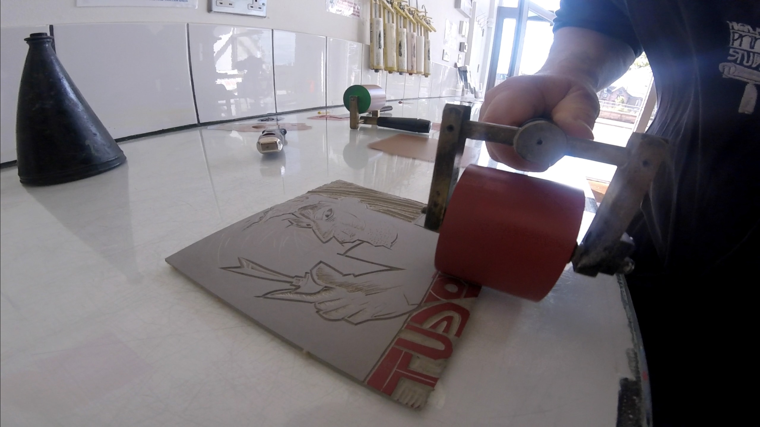 A person inking up the relief plate using rollers of ink