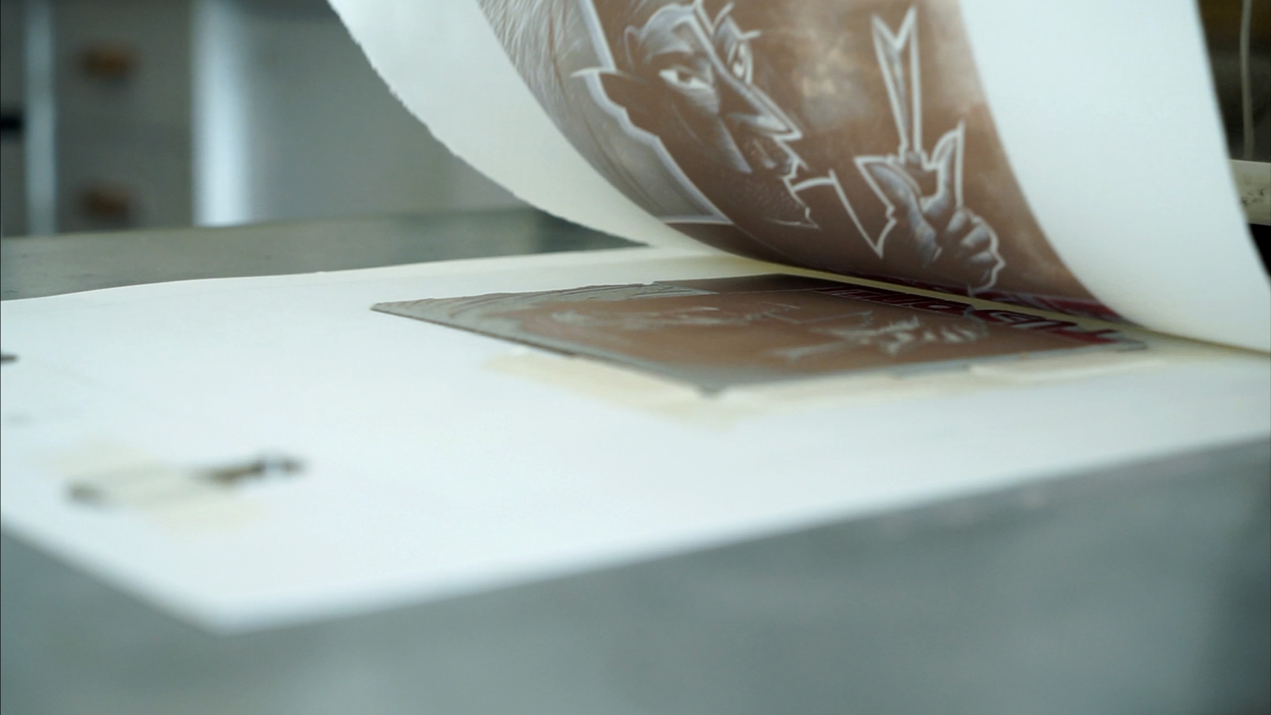 A relief print being completed with the relief being peeled away from the paper